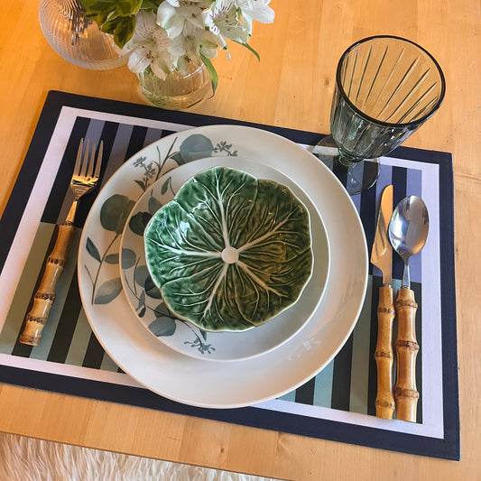 Table setting with a decorative plate featuring a green leaf design on a striped placemat.