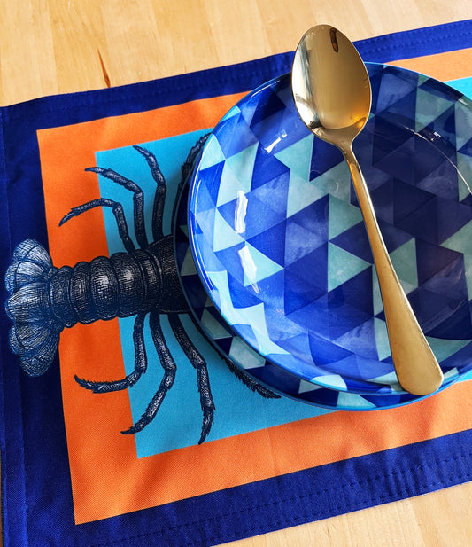 Napkin with lobster design on a blue plate with geometric pattern and gold spoon