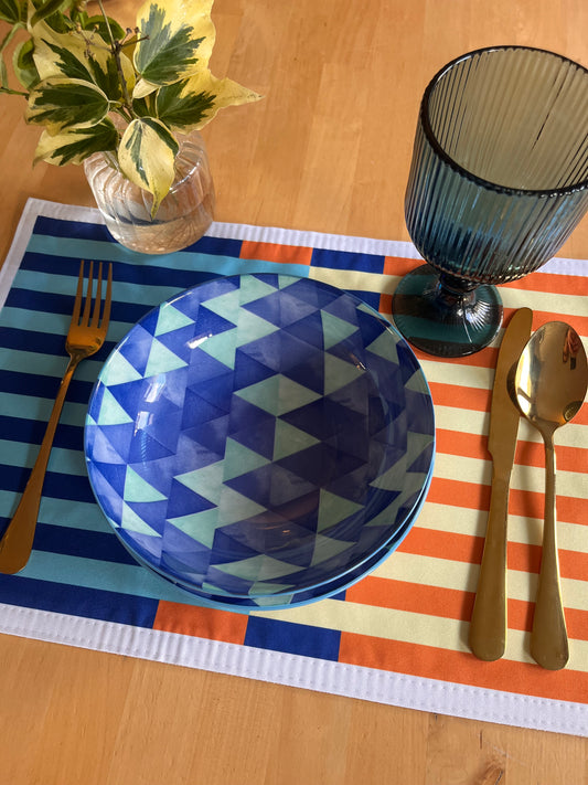 Blue geometric-patterned plate on a striped placemat with cutlery and a glass.
