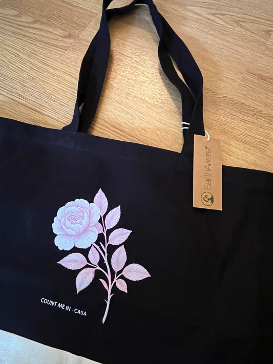 Charcoal Peony organic cotton shopping bag by Count Me In - Casa with a pink peony graphic, on a wooden floor