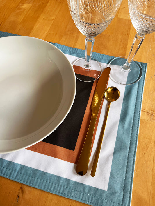 Dining table setting with a white plate, gold cutlery, and crystal glasses on a blue exclusive design placemat.