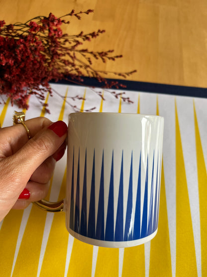 Hand holding a blue and white mug with a decorative pattern on a yellow and white striped background.