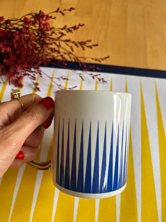 Hand holding a blue and white mug with a decorative pattern on a yellow and white striped background.