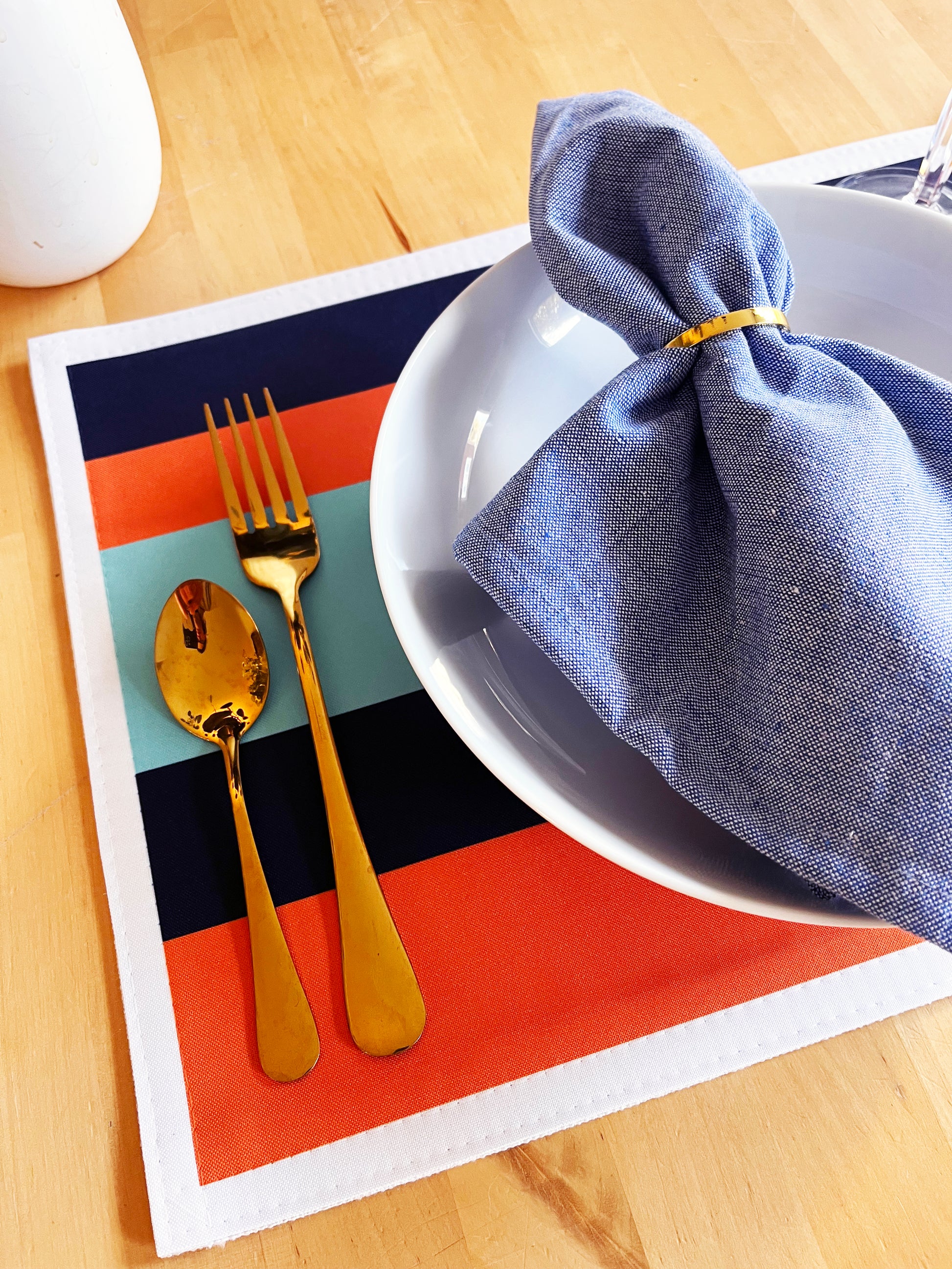 Colorful placemat with gold cutlery and a blue napkin on a wooden table.