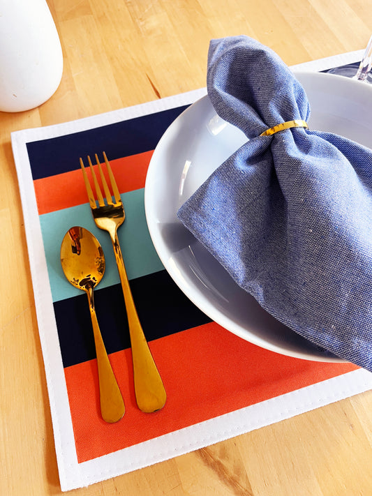 Colorful placemat with gold cutlery and a blue napkin on a wooden table.