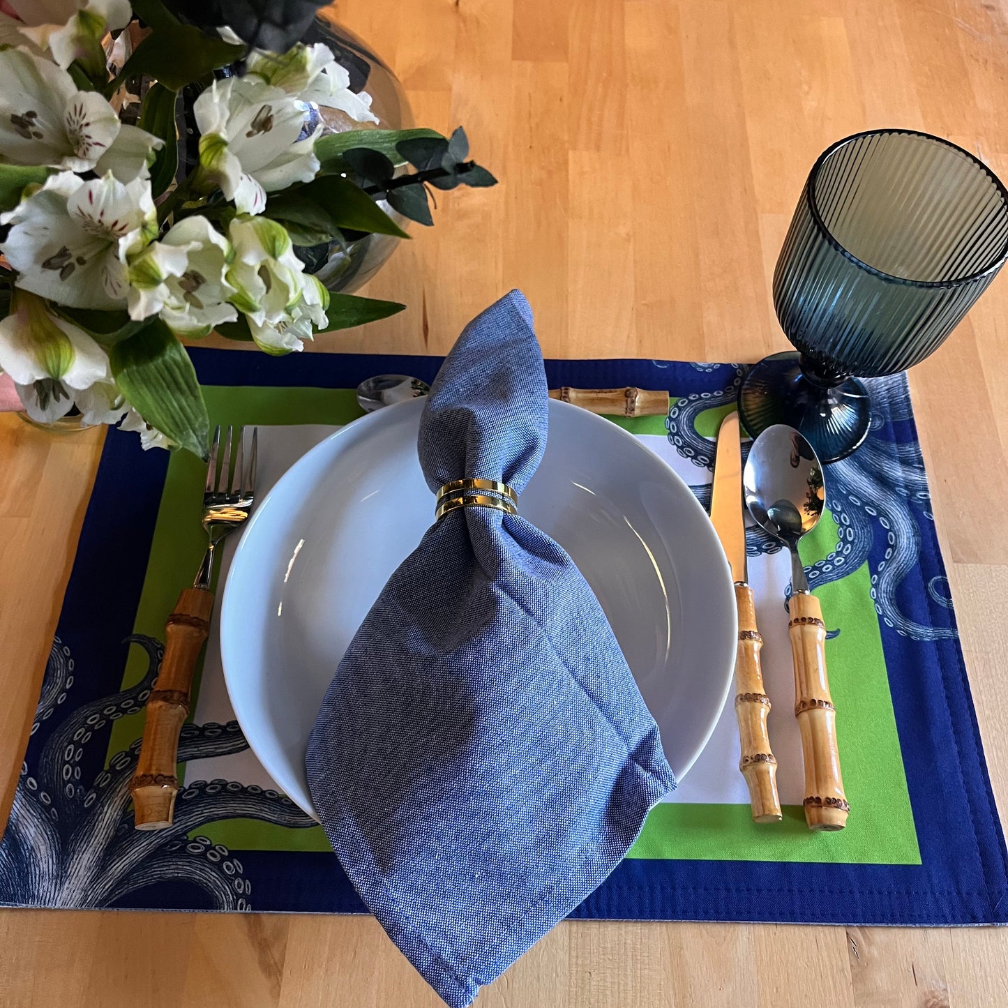 Dining table setting with a white plate, blue napkin, and floral arrangement.