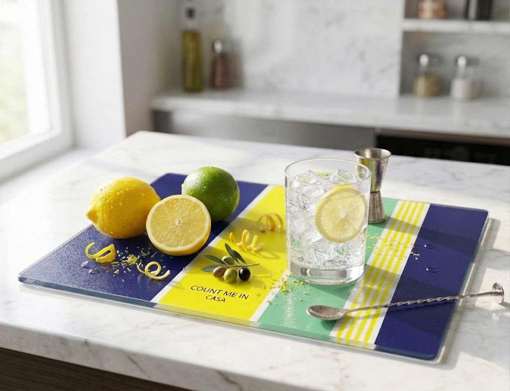 Colorful cutting board or cheese board with lemons, a glass of water, and a spoon on a kitchen counter.