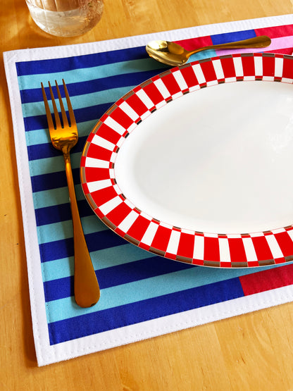 Red and white striped plate with gold fork on a blue, pink and red striped placemat designed in the uk, exclusive placemat detailed image. Zoom of the product