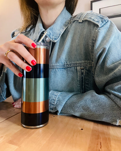 Person holding a striped colour blocking graphic tumbler on a wooden floor. 