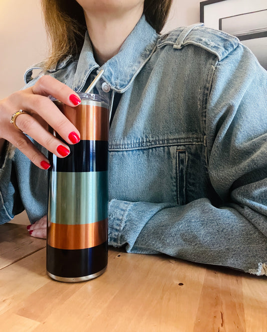 Person holding a striped colour blocking graphic tumbler on a wooden floor. 