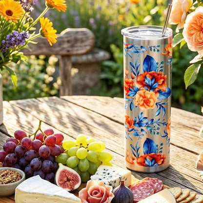 Floral-patterned tumbler on a wooden table with a charcuterie board and flowers in the background.