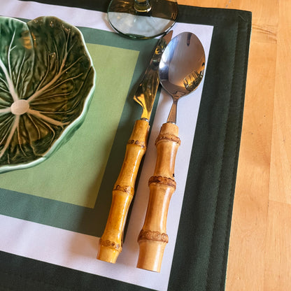 Bamboo-handled spoon and fork on a green and white placemat with a Bordallo Pinheiro ceramic leaf-patterned bowl.