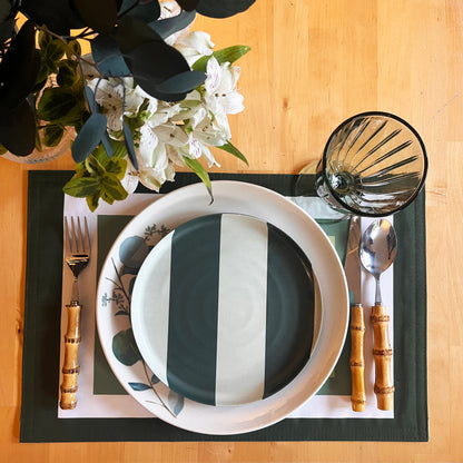 Place setting with black and white striped plate, bamboo cutlery, and white and green floral arrangement on a wooden table, refined placemat from the Frame collection