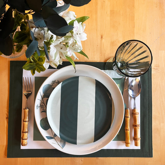 Place setting with black and white striped plate, bamboo cutlery, and white and green floral arrangement on a wooden table, refined placemat from the Frame collection