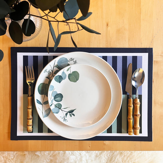 Dinner setting with floral-patterned plates, bamboo cutlery, and a green and blue striped placemat on a wooden table.
