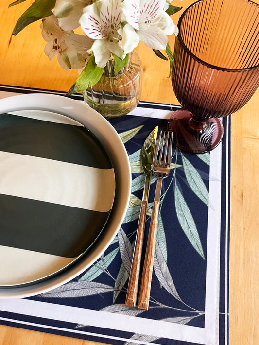 Table setting with striped plate, floral arrangement, and cutlery on a leaf-patterned placemat.