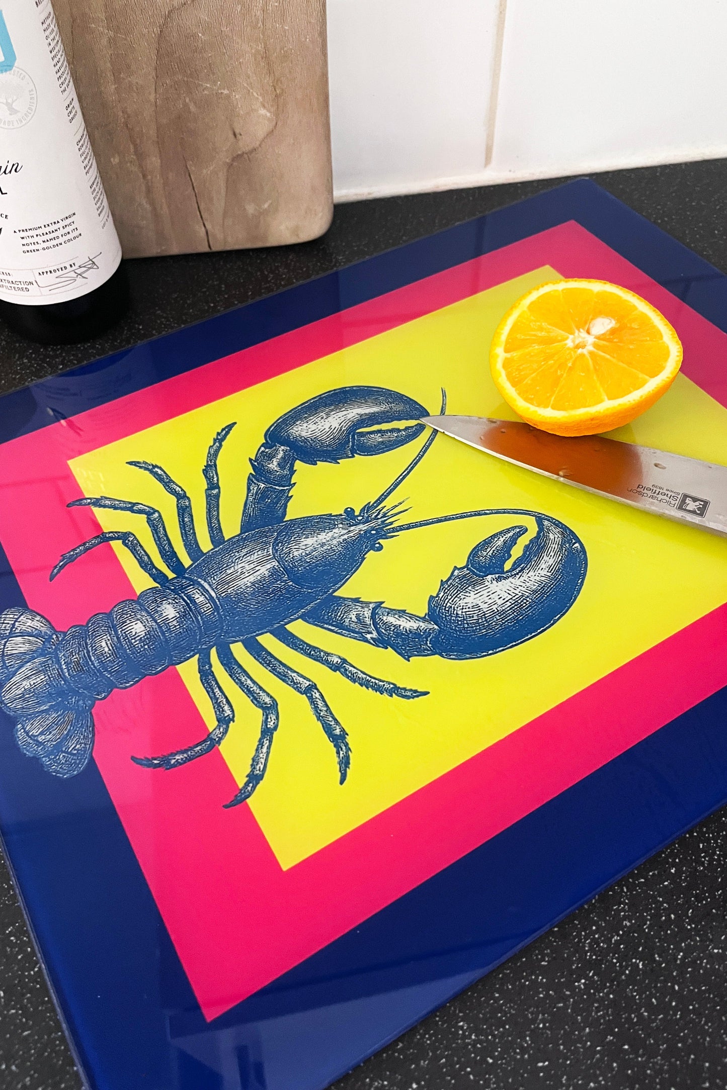 Colorful cutting board with an exclusive lobster design, knife, and half an orange on a kitchen counter.