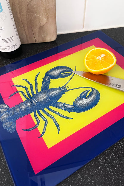 Colorful cutting board with an exclusive lobster design, knife, and half an orange on a kitchen counter.