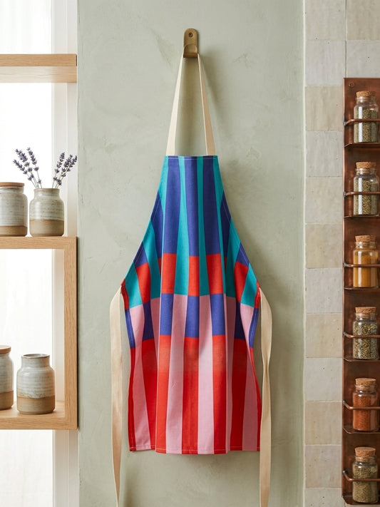 A colorful apron with vertical stripes in red, pink, blue, and teal hangs on a wooden peg on a textured wall in a kitchen setting.
