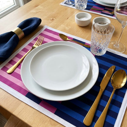 Dining table setting with white plates, gold cutlery, and striped placemats.