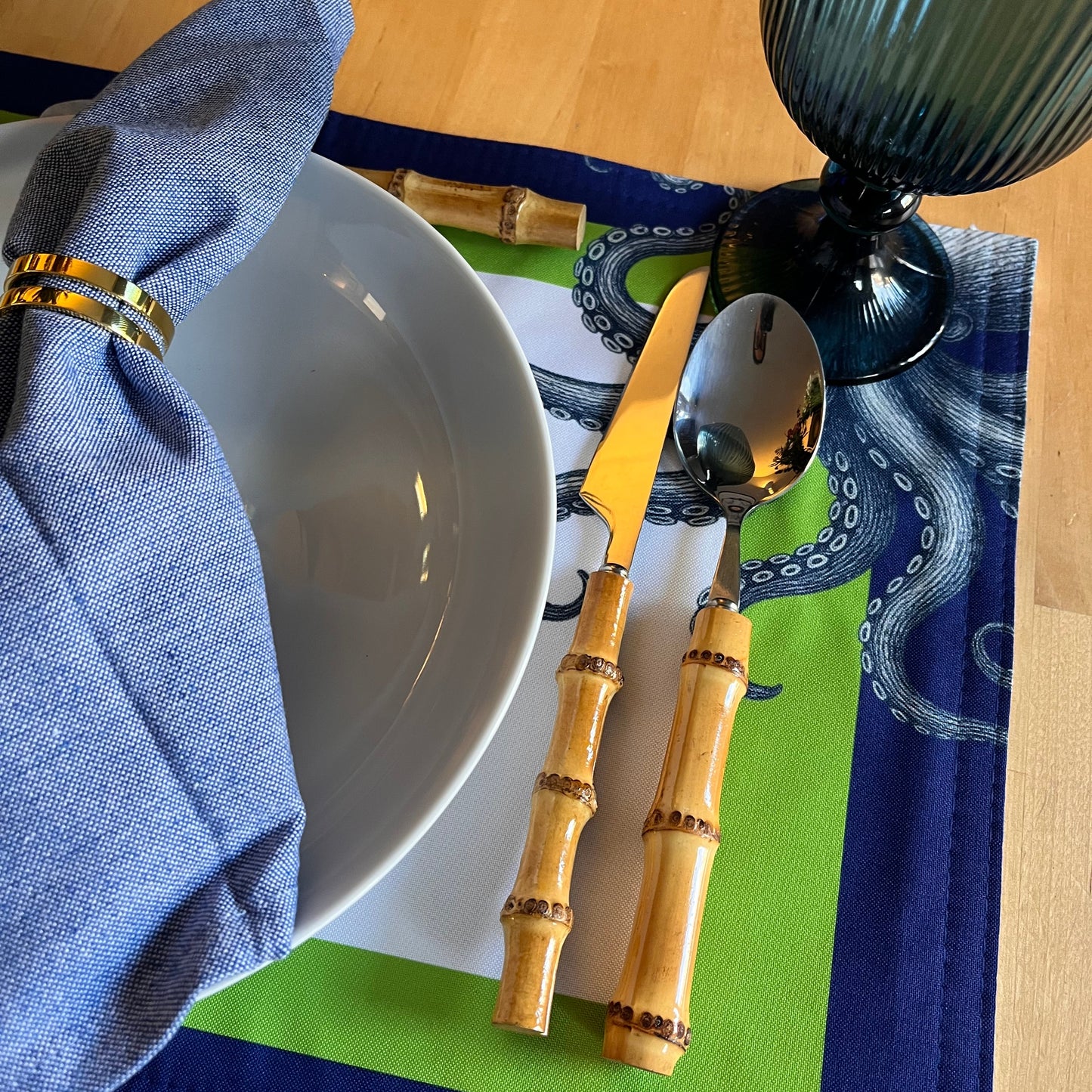 Bamboo cutlery set on a table with a blue napkin and a white bowl. Beautiful octopus-themed placemat.