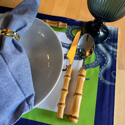 Bamboo cutlery set on a table with a blue napkin and a white bowl. Beautiful octopus-themed placemat.