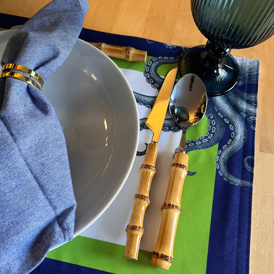 Bamboo cutlery set on a table with a blue napkin and a white bowl. Beautiful octopus-themed placemat.