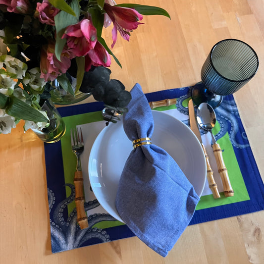 Dining table setting with a blue napkin, white plate, and floral arrangement.