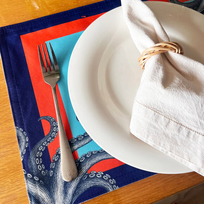 White plate with a folded white napkin, fork, and colorful placemat on a wooden table.