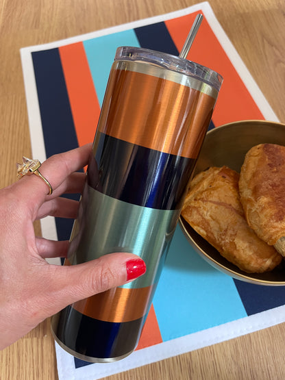 Hand holding a striped tumbler with a colorful mat and pastries in the background