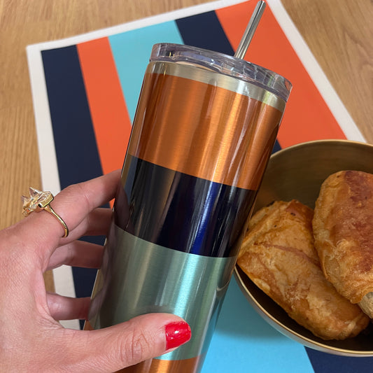 Hand holding a striped tumbler with a colorful mat and pastries in the background