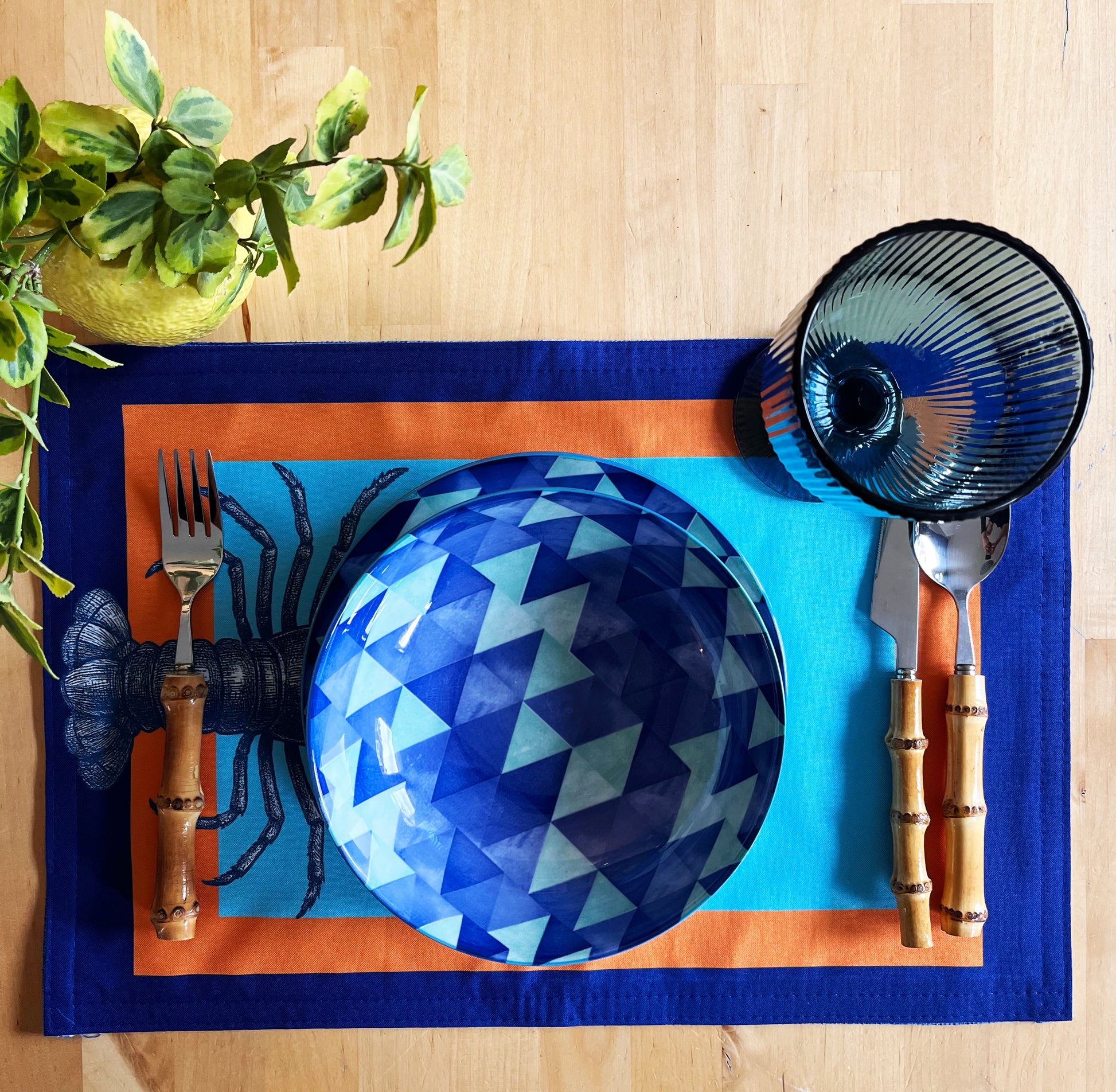 Blue geometric-patterned plate on a blue placemat with cutlery and a plant on a wooden surface