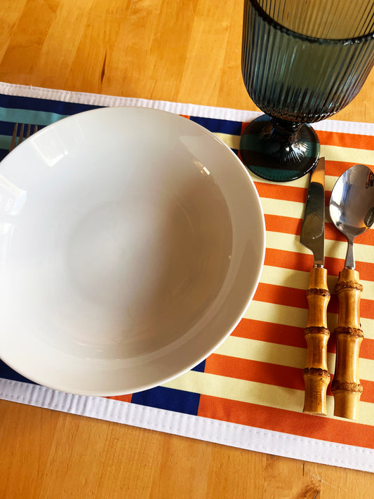 White bowl on a striped placemat with a glass and cutlery set. Exclusive design.
