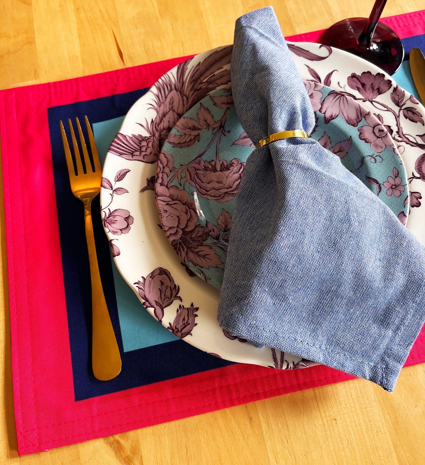 Dining setup with floral plates, blue napkin, and cutlery on a colorful placemat with an exclusive design, high quality.