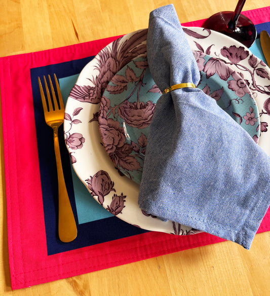 Dining setup with floral plates, blue napkin, and cutlery on a colorful placemat with an exclusive design, high quality.