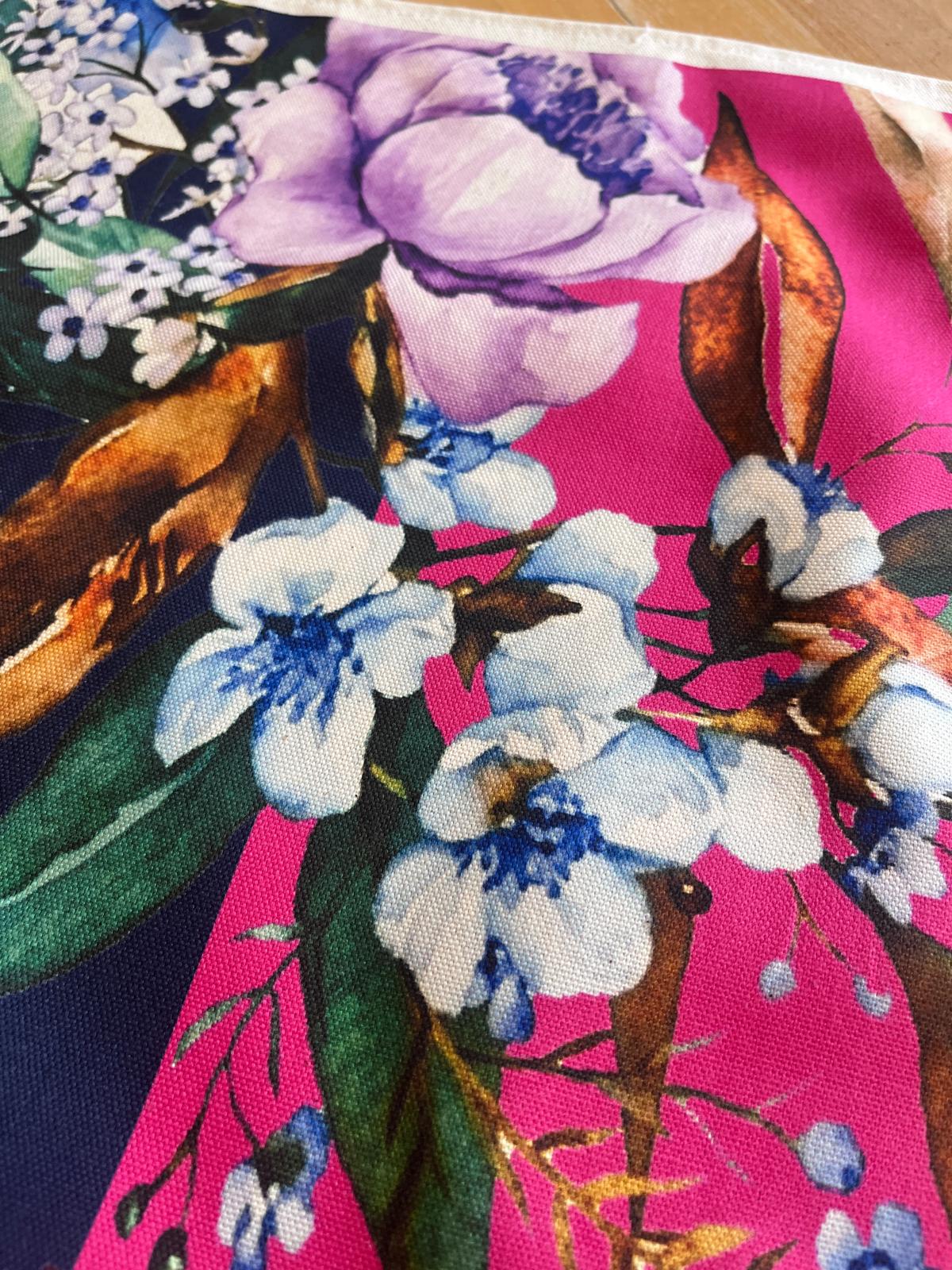 A close-up of a colorful floral fabric print featuring large purple flowers, white blossoms with blue centers, green leaves, and brown branches on a vivid pink background.