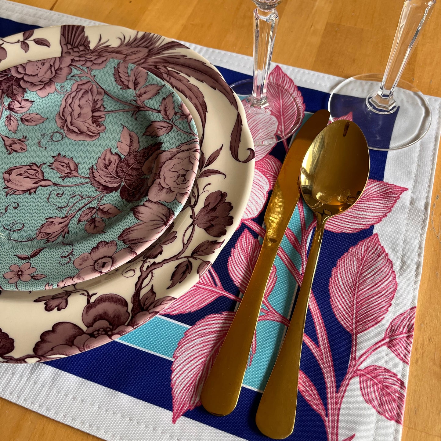 Set of floral-patterned plates on a decorative placemat with cutlery and glasses, exclusive design