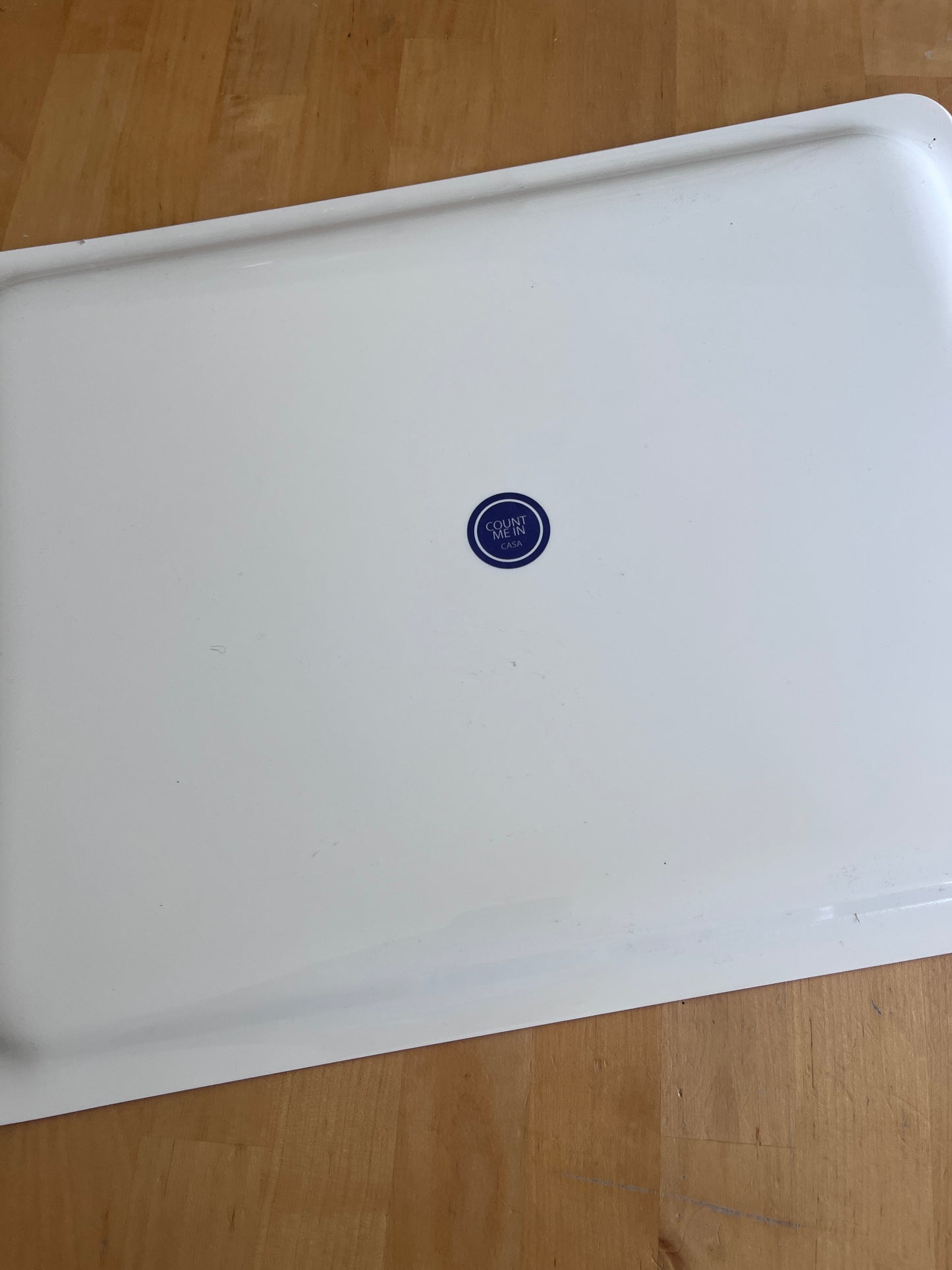 A white enamel or metal baking pan with a small blue circular 35 oz logo in the center, photographed from above on a light wood floor.