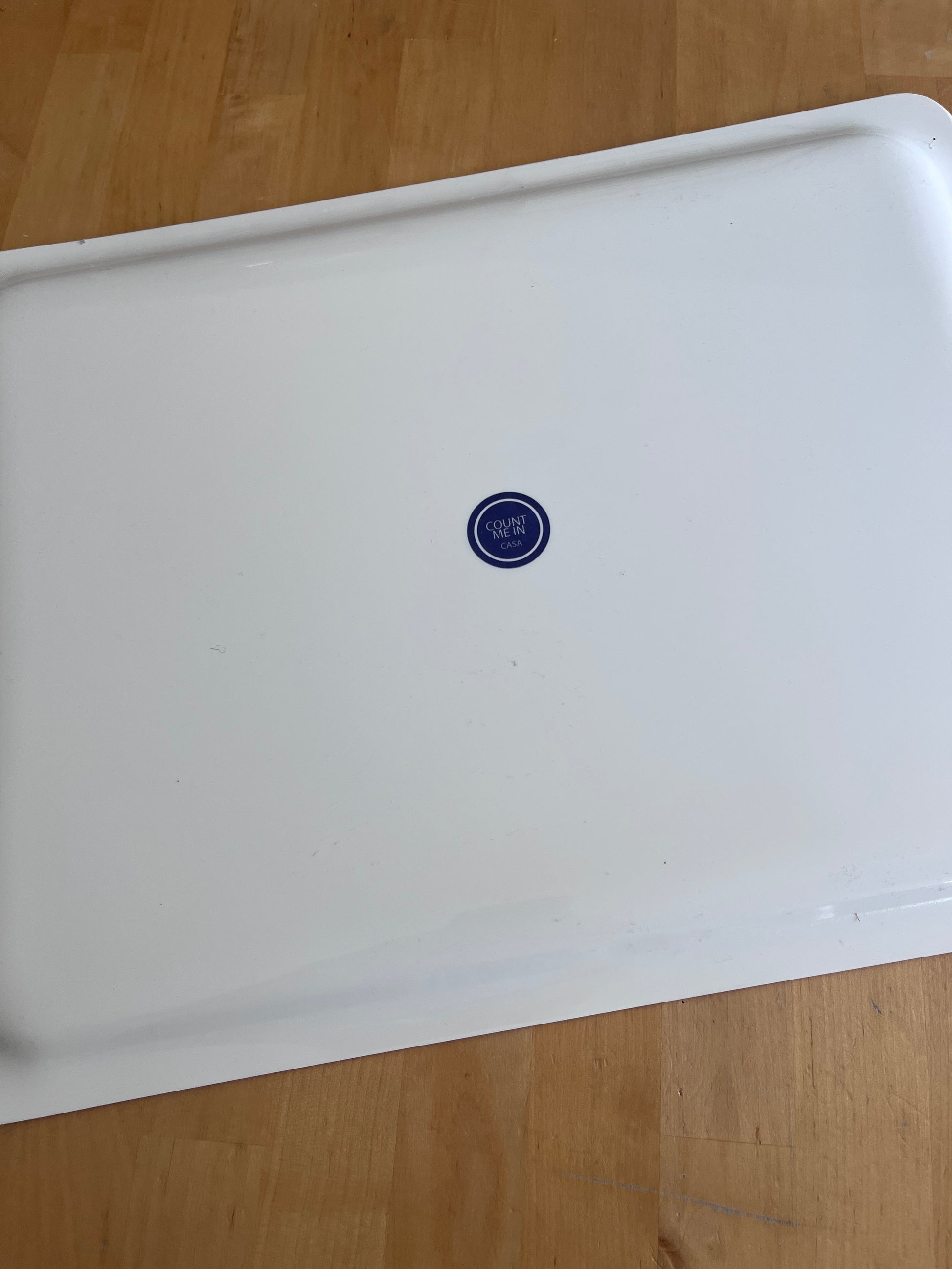 A white enamel or metal baking pan with a small blue circular 35 oz logo in the center, photographed from above on a light wood floor.