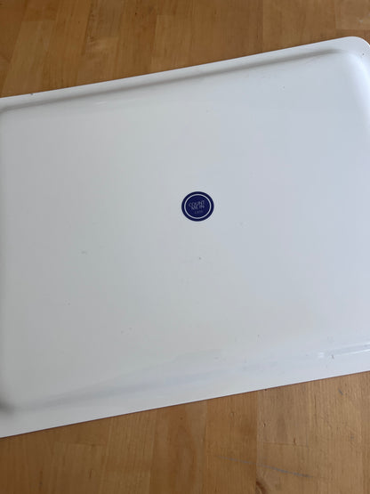 A white enamel or metal baking pan with a small blue circular 35 oz logo in the center, photographed from above on a light wood floor.