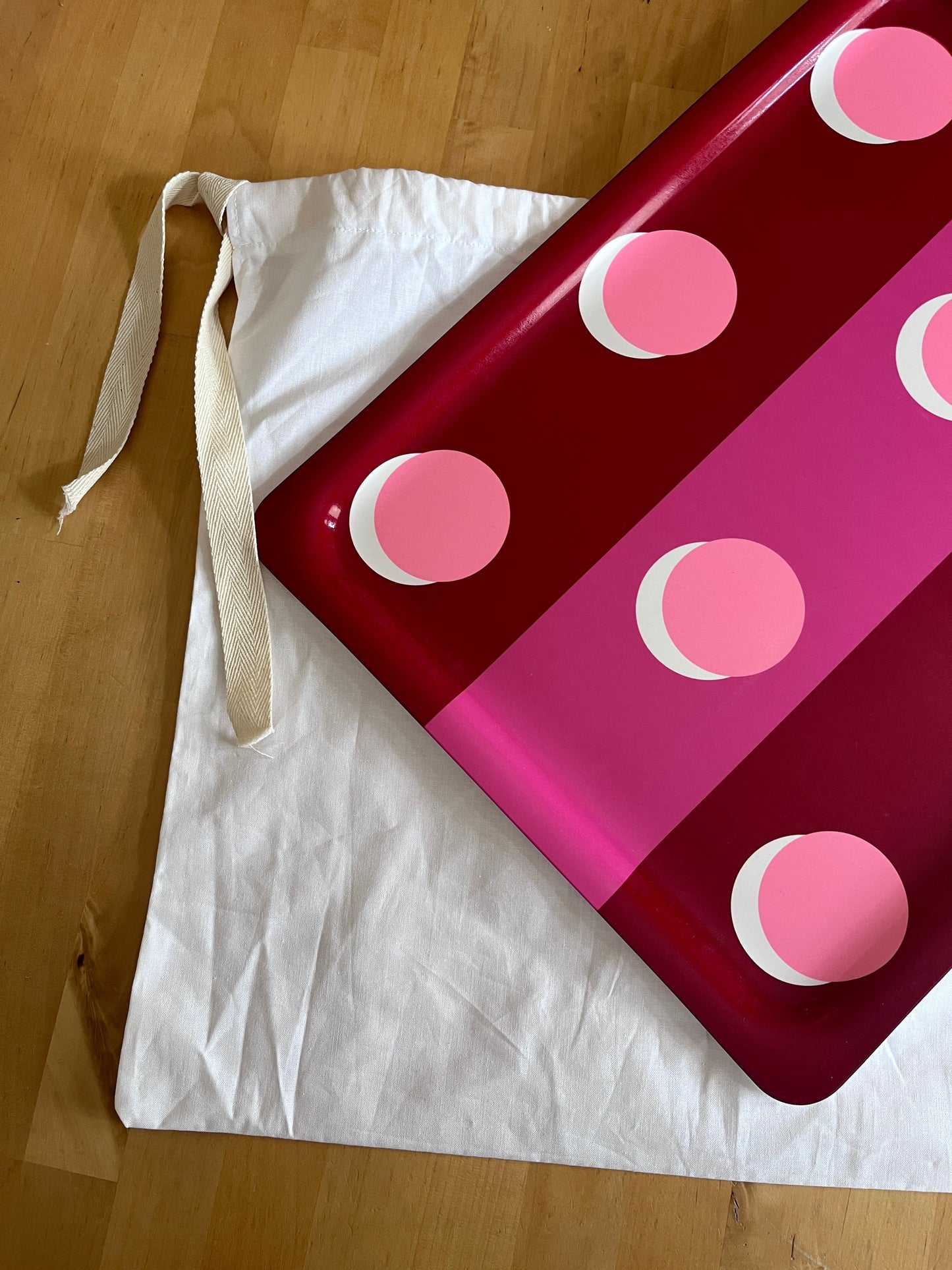 A glossy red and pink polka-dot tray or serving board placed diagonally over a white canvas tote bag on a light wood floor.