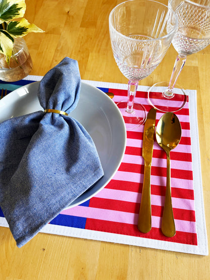 Dinner setting with blue napkin, white plate, gold cutlery, and red and white striped placemat on a wooden table.A stylish, versatile collection designed for modern table settings, home décor lovers, and anyone who enjoys effortless creativity.