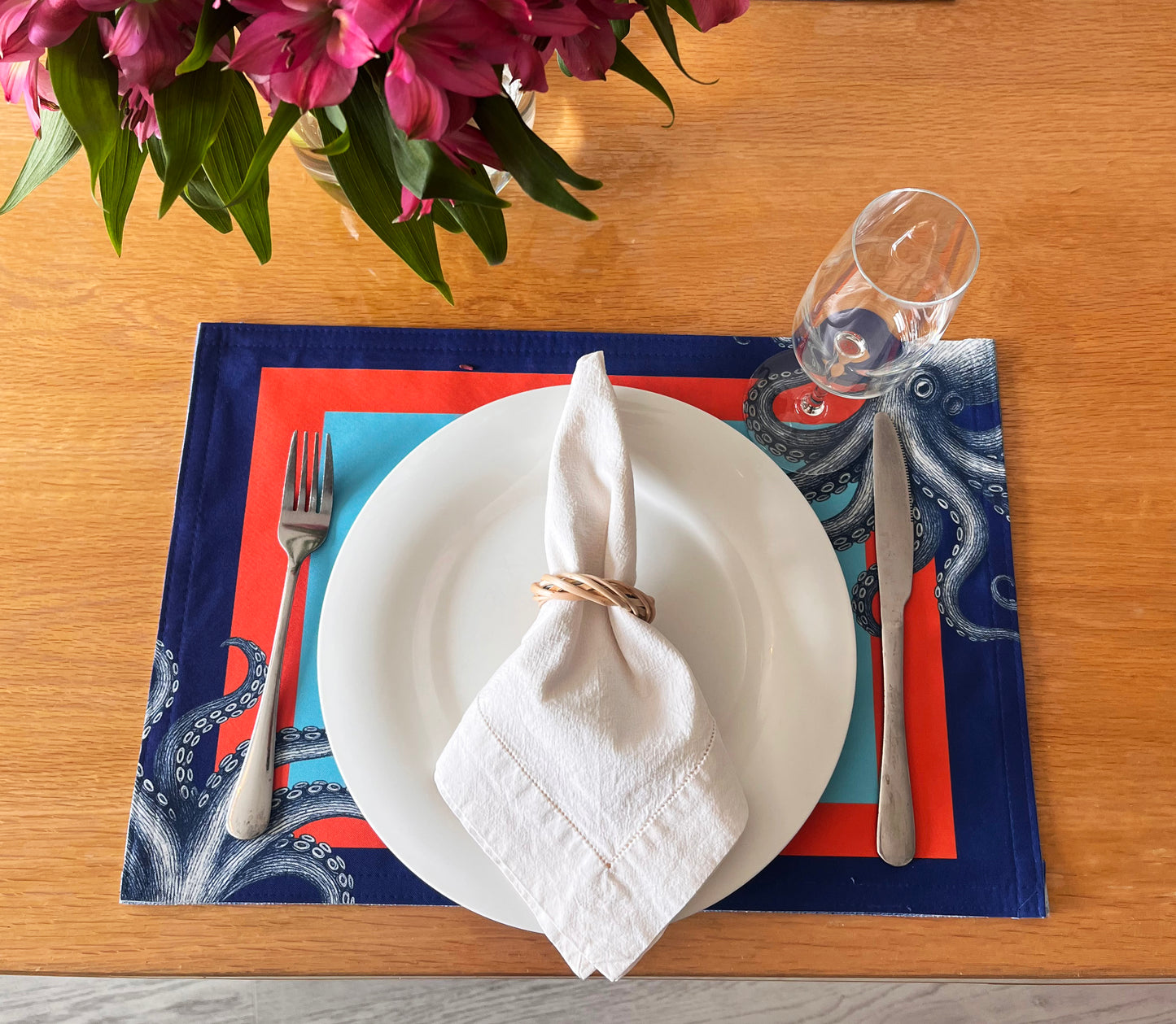 Set table with white plate, napkin, and cutlery on a decorative placemat with flowers in the background.
