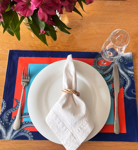Set table with white plate, napkin, and cutlery on a decorative placemat with flowers in the background.