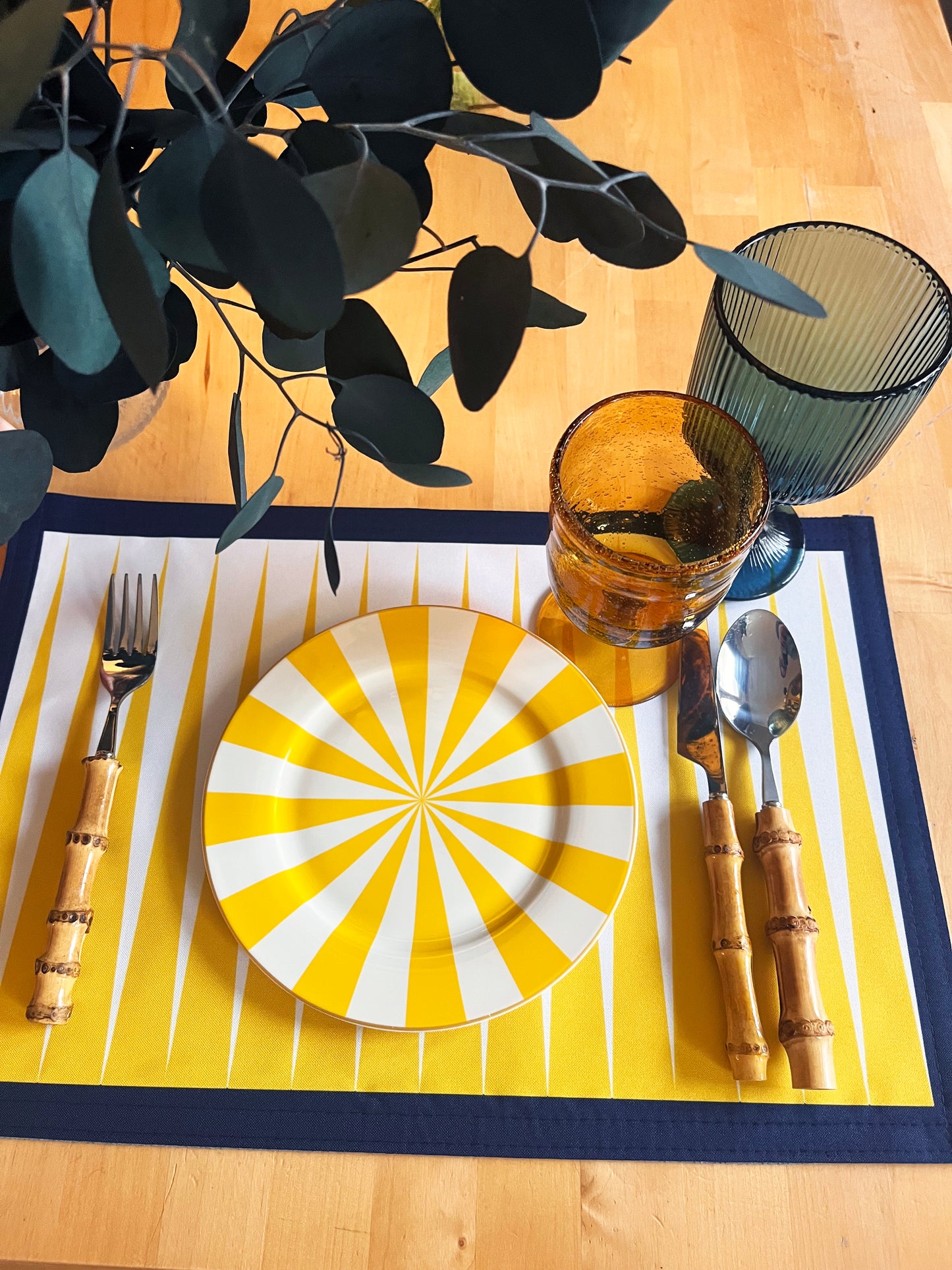 Dining table setting with yellow and white striped plate, cutlery, and glass on a striped placemat.