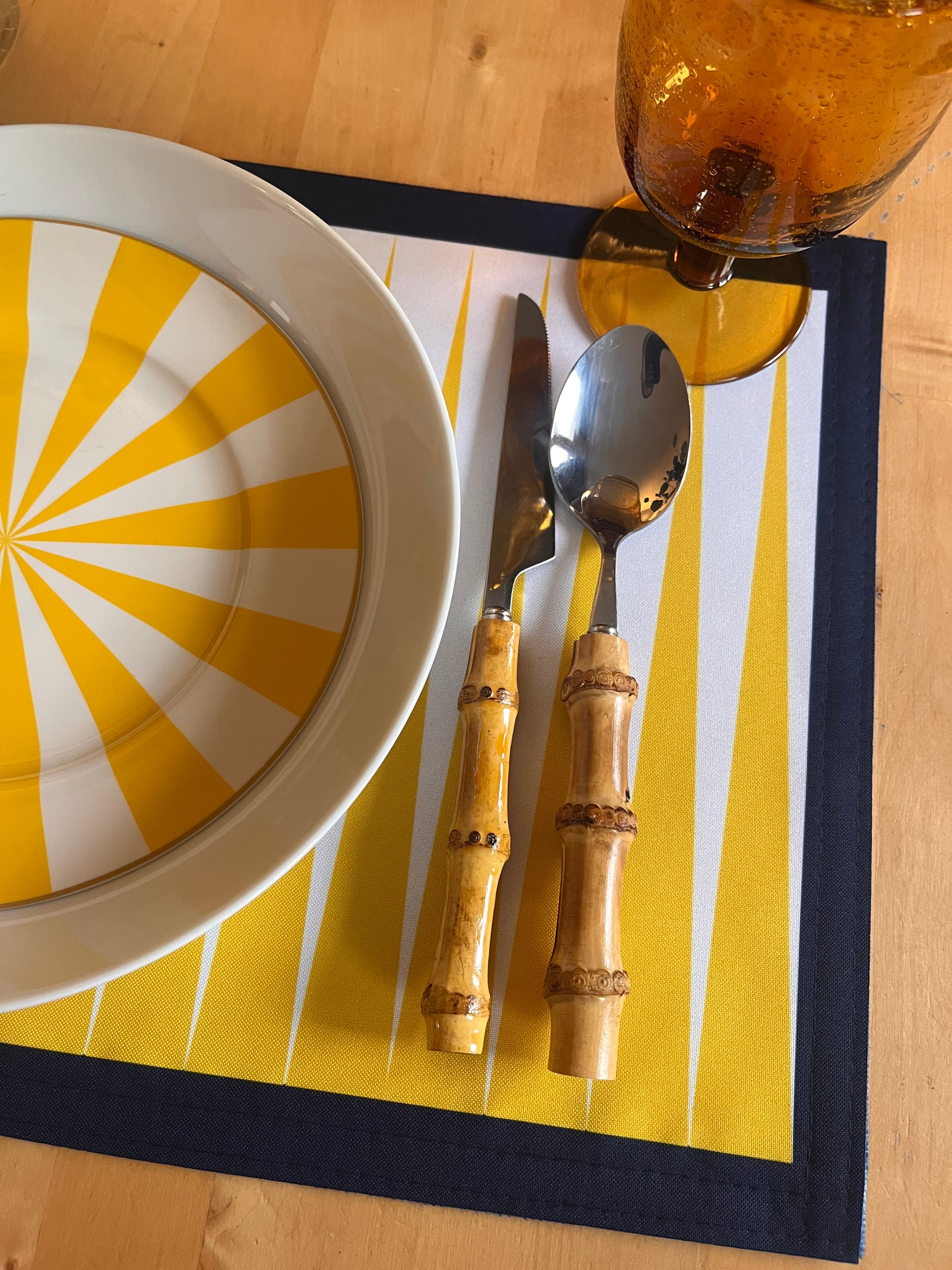 Dinner set with yellow and white plate, knife, and spoon on a yellow placemat in detail. 