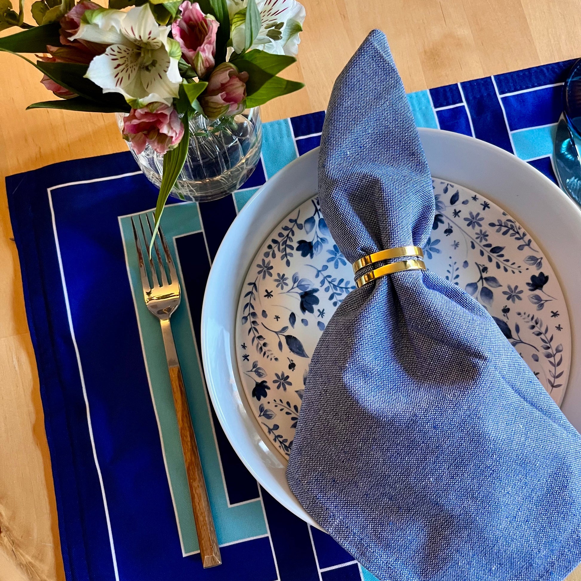 Dining table setting with blue napkin, floral arrangement, decorative plates, and an exclusive design placemat.