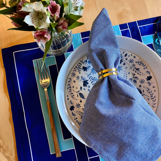Dining table setting with blue napkin, floral arrangement, decorative plates, and an exclusive design placemat.