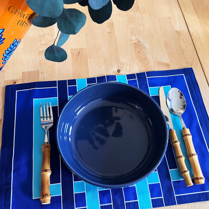 Blue plate with bamboo cutlery on a blue placemat on a wooden table, plants, and a beautiful natural mood.