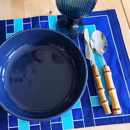 Blue plate, glass, knife, and spoon on a blue graphic design placemat with a wooden surface.